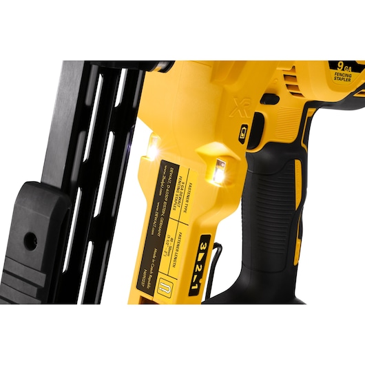 Close-up of yellow DEWALT fencing stapler handle with LED lights and safety labels visible.