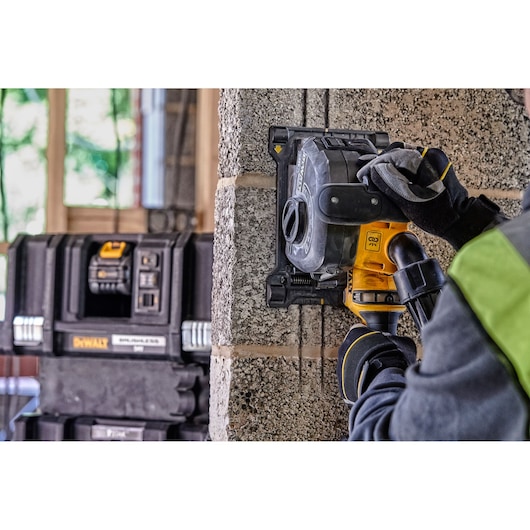 Person using a DEWALT wall chaser tool to cut slots in a concrete wall, with DEWALT toolboxes in the background.