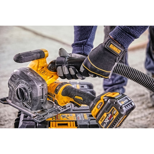 A close-up view of a person wearing gloves and connecting a hose to a DEWALT cordless wall chaser, model DCG200T2, placed on a DEWALT toolbox.