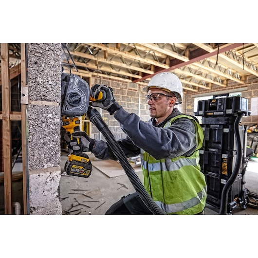 Person using a DEWALT DCG200T2 power tool to cut concrete wall at a construction site, wearing safety gear.