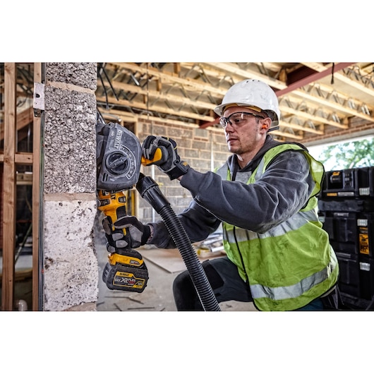 Worker uses DEWALT DCG200T2 wall chaser tool on concrete wall at construction site, wearing safety gear.