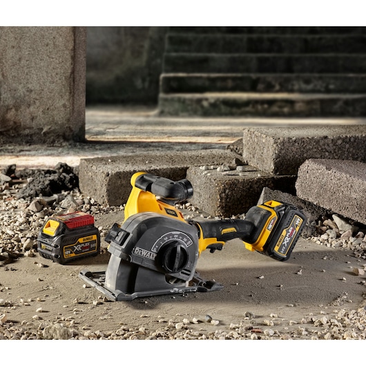 A DEWALT cordless wall chaser tool with battery, placed on a construction site floor surrounded by concrete debris and slabs.