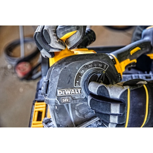 Gloved hands adjust a DEWALT 54V power tool with a dial, showing rugged construction and brand label.