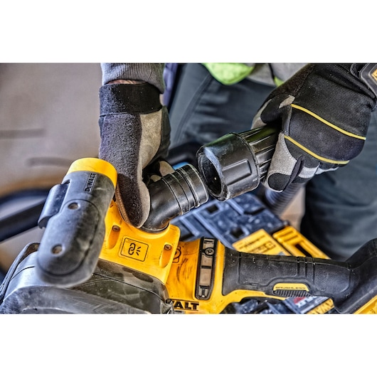 Gloved hands attach a hose to a yellow DEWALT power tool, shown in close-up during use.