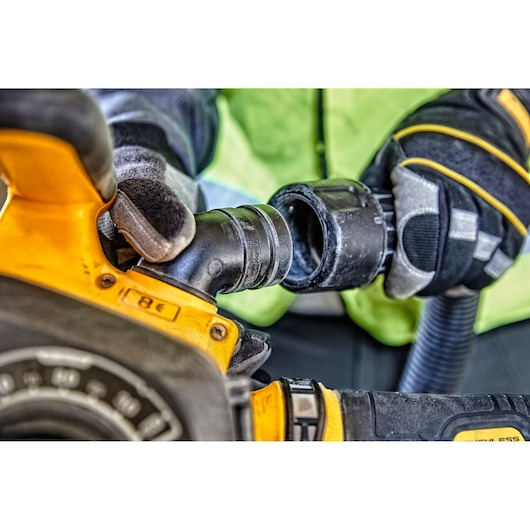 Gloved hands connect a hose to a yellow DEWALT power tool during use.