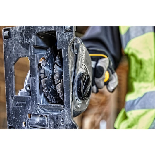 Close-up of a DEWALT power tool in use, held by a gloved hand wearing a safety vest.