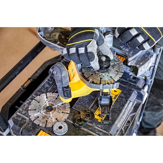 Gloved hands adjusting circular saw blades and attachments on a yellow DEWALT tool box.
