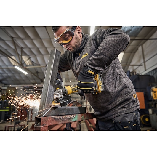 Man uses DEWALT grinder DCG404NT, DCG404S2T-QW on metal, sparks flying, in workshop.