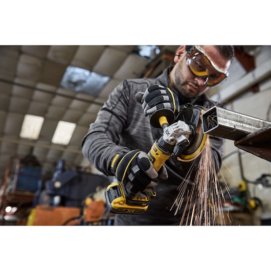 DEWALT DCG404NT, DCG404S2T-QW: worker grinding metal, sparks flying, industrial setting.