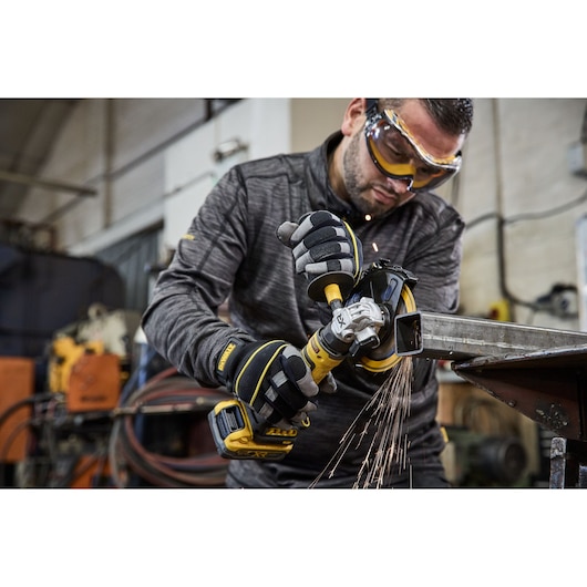 DEWALT DCG404NT and DCG404S2T-QW in use grinding metal, sparks flying, operator wearing gloves.