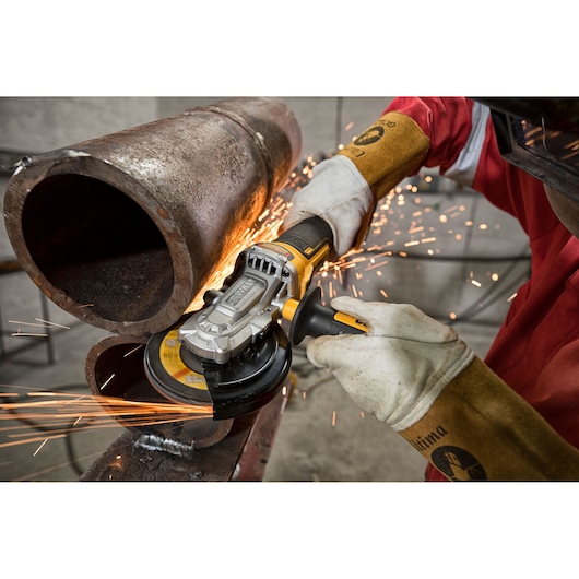 Person uses a DEWALT angle grinder to cut a metal pipe, creating sparks in an industrial setting.