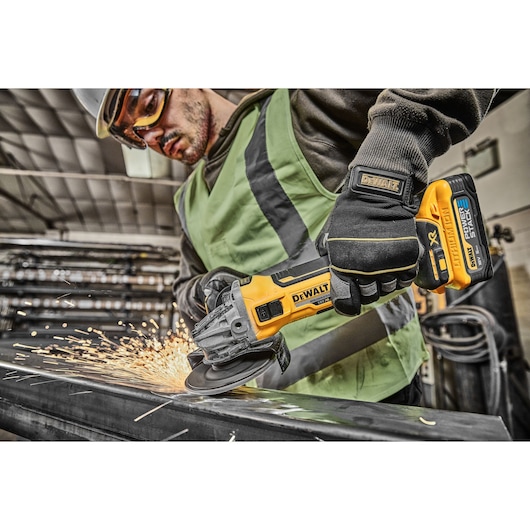 Worker uses DEWALT cordless grinder, producing sparks while grinding metal in an industrial environment.