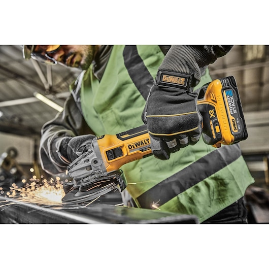 Person using a DEWALT cordless grinder on metal, sparks flying, in a workshop setting.