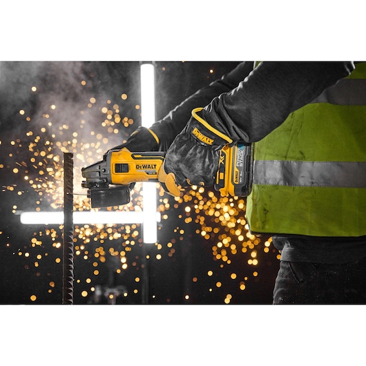 Person using DEWALT cordless grinder to cut metal with sparks, wearing gloves and a safety vest.