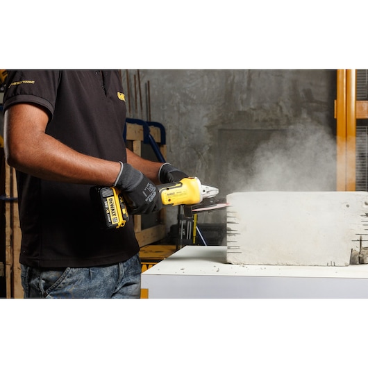 Person using a DEWALT cordless angle grinder on a concrete block, producing dust indoors.