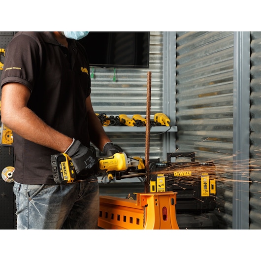 Person uses a DEWALT cordless grinder to cut metal, with sparks visible in a workshop setting.
