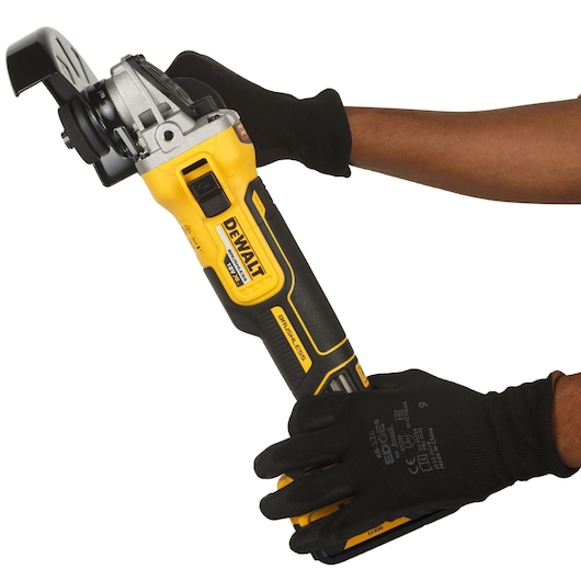 A person wearing black gloves is holding a yellow and black DEWALT cordless angle grinder.