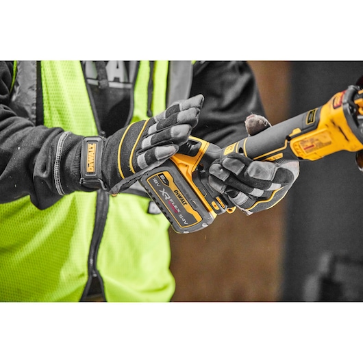 Person wearing gloves holds a DEWALT XR FlexVolt cordless power tool in a workshop setting.