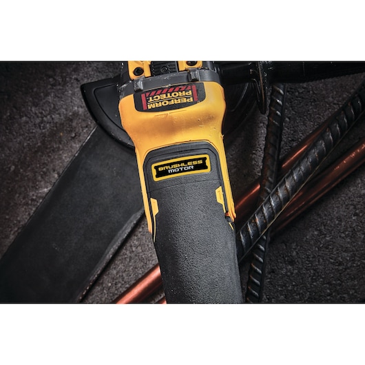 Close-up view of a DEWALT power tool with a yellow and black body, featuring a 'Brushless Motor' label and a 'Perform Protect' sticker. The tool is placed on a rough surface alongside metal rods.