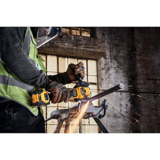 Worker uses DEWALT cordless angle grinder to cut metal rebar, sparks flying at industrial jobsite.