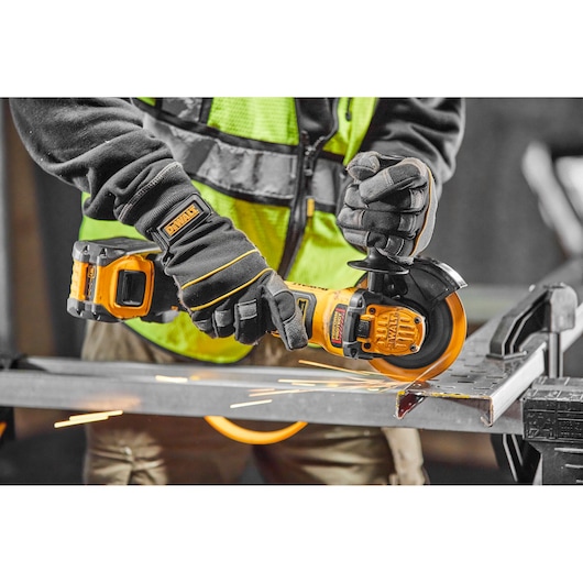 Person uses DEWALT cordless grinder on metal, wearing gloves and safety vest with visible sparks.