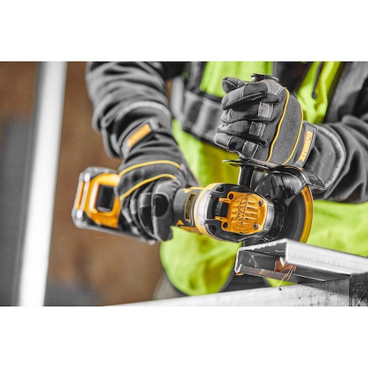Person using DEWALT cordless angle grinder to cut metal, wearing gloves and safety vest.