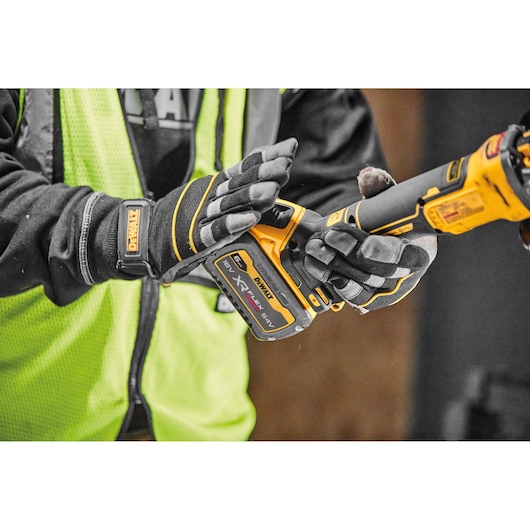 Person with gloves holds a DEWALT cordless XR FLEXVOLT power tool, wearing a yellow safety vest.