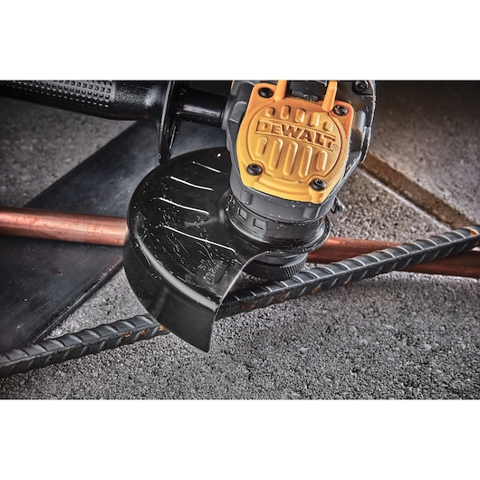 DEWALT cordless grinder cutting metal rebar on a rough concrete surface.