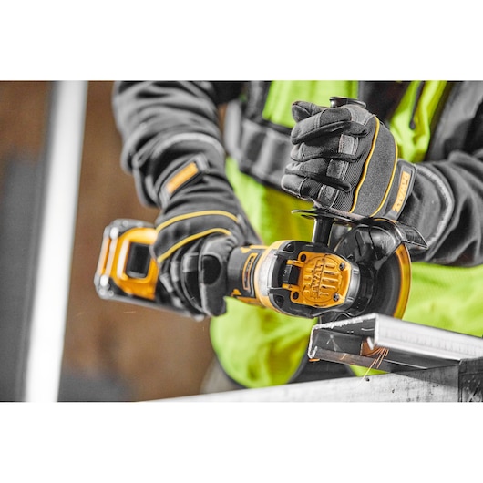 Person using DEWALT cordless grinder with gloves to cut metal on a workbench.