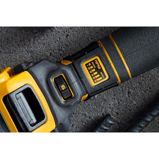 Close-up of a DEWALT power tool with RPM settings and adjustment dial, placed on a textured concrete surface.