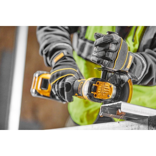 Person using a DEWALT cordless grinder to cut metal, wearing gloves and safety vest.
