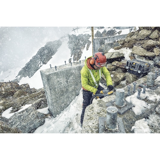 Worker in snow uses DEWALT tool on concrete, mountains in background, DEWALT toolbox visible.