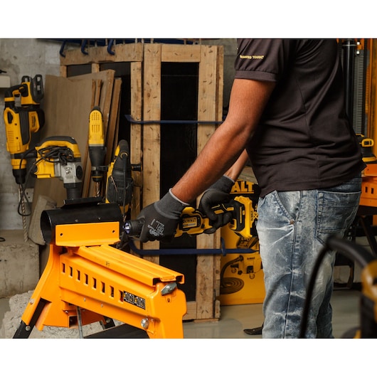 Person uses DEWALT DCG426P2 tool on orange workbench in workshop with other power tools visible in the background.