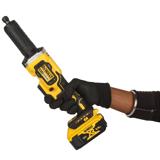 A gloved hand holding a yellow and black DEWALT cordless die grinder with an 18V XR lithium-ion battery.