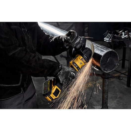 Person using a DEWALT grinder to cut a metal pipe, sparks flying in an industrial setting.