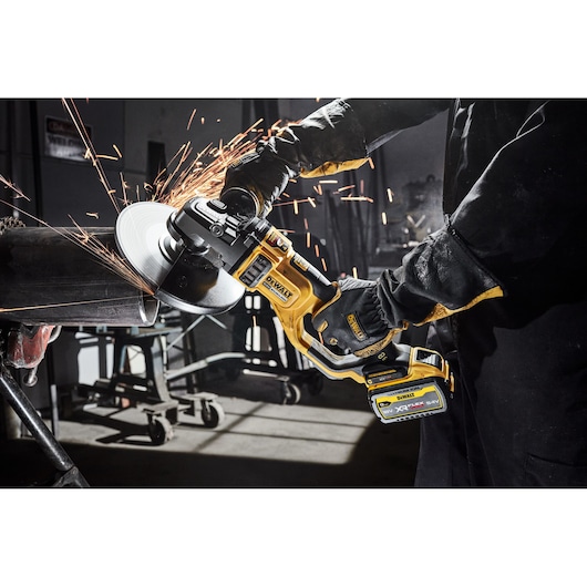 DEWALT cordless grinder cutting metal with sparks in workshop. Worker wearing gloves and protective clothing.