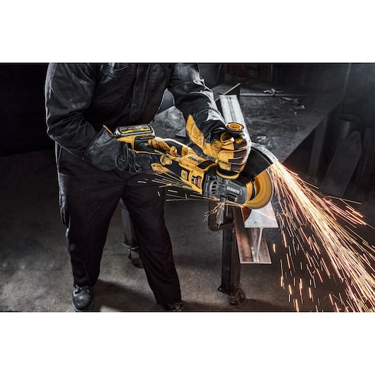 Person uses DEWALT cordless grinder, producing bright sparks while working on metal in industrial setting.