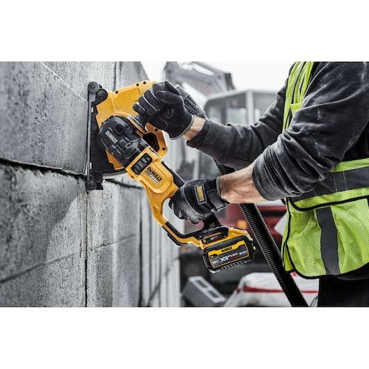 Worker using a DEWALT cordless wall chaser to cut grooves in a concrete block wall on a construction site.