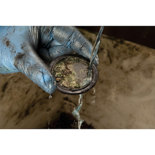 A close-up of a gloved hand holding a dirty mesh filter while water is being poured over it to clean debris.