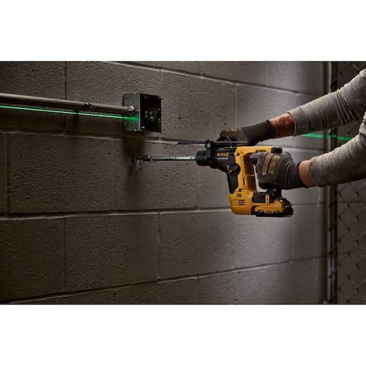 Person using a DEWALT rotary hammer drill on a concrete wall next to electrical conduit.