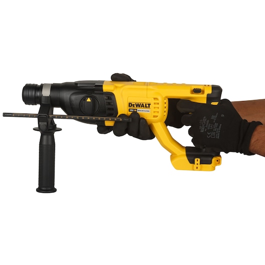 A DEWALT cordless rotary hammer drill (model DCH133NT-XJ) being held in gloved hands, featuring a yellow and black design with side handle and depth rod.