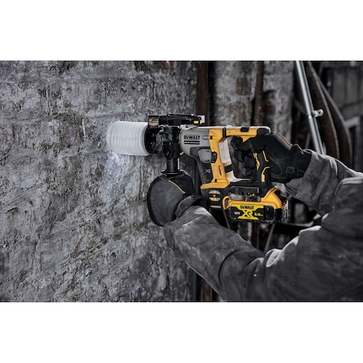 Person using a DEWALT cordless rotary hammer drill to bore into a concrete wall at a construction site.