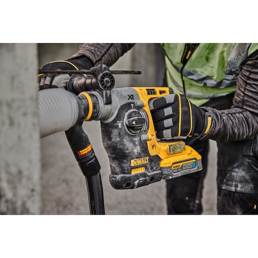A close-up of a worker using a DEWALT cordless rotary hammer drill with a POWERSTACK battery to drill into concrete, wearing protective gloves and clothing.