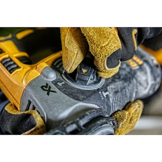 Gloved hand adjusting control on a yellow DEWALT power tool with visible function icons.