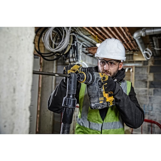 Worker in safety gear using a DEWALT DCH274P2T rotary hammer drill on a construction site.