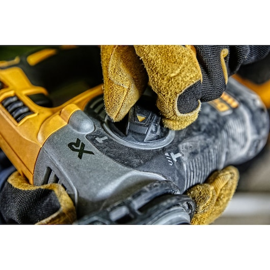 Gloved hand adjusting control on a yellow DEWALT power tool with visible function icons.