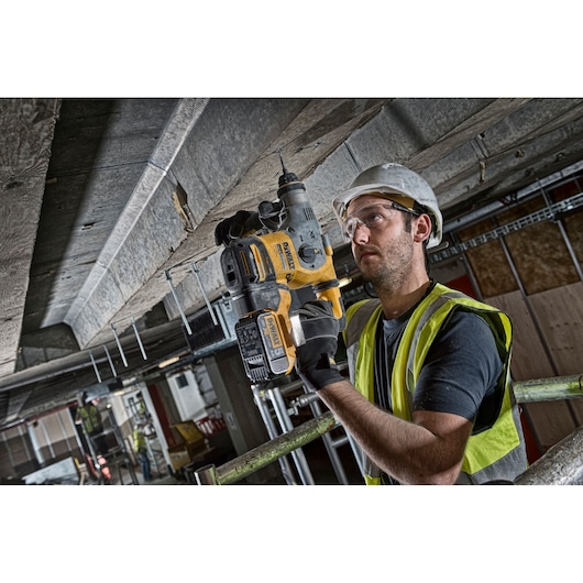 Worker using DEWALT DCH283P2 rotary hammer drill for ceiling installation in a construction environment.
