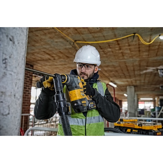 Worker uses a DEWALT rotary hammer drill on a construction site, wearing safety gear and gloves.