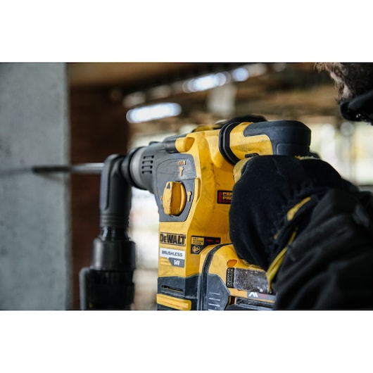 Person using a DEWALT DCH323NT brushless rotary hammer drill on concrete at a construction site.