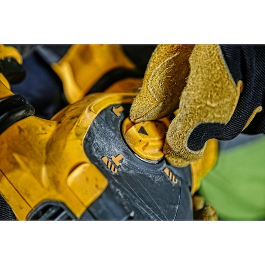 Gloved hand adjusts the mode selector on a yellow DEWALT power tool, showing detailed closeup of switch and icons.